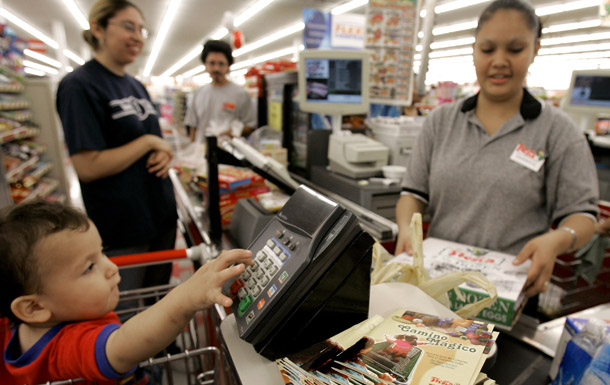 Matthew Alacon, 1, plays at the register as clerk Jessica Martinez, right, checks out Isabel Mendoza's groceries at a grocery store in Houston. (AP/Pat Sullivan)