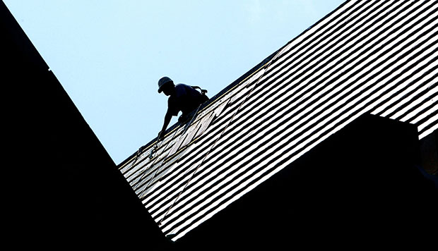 A construction worker is silhouetted by the morning sun as he works on the roof of a college, July 2004. (AP/Phil Coale)
