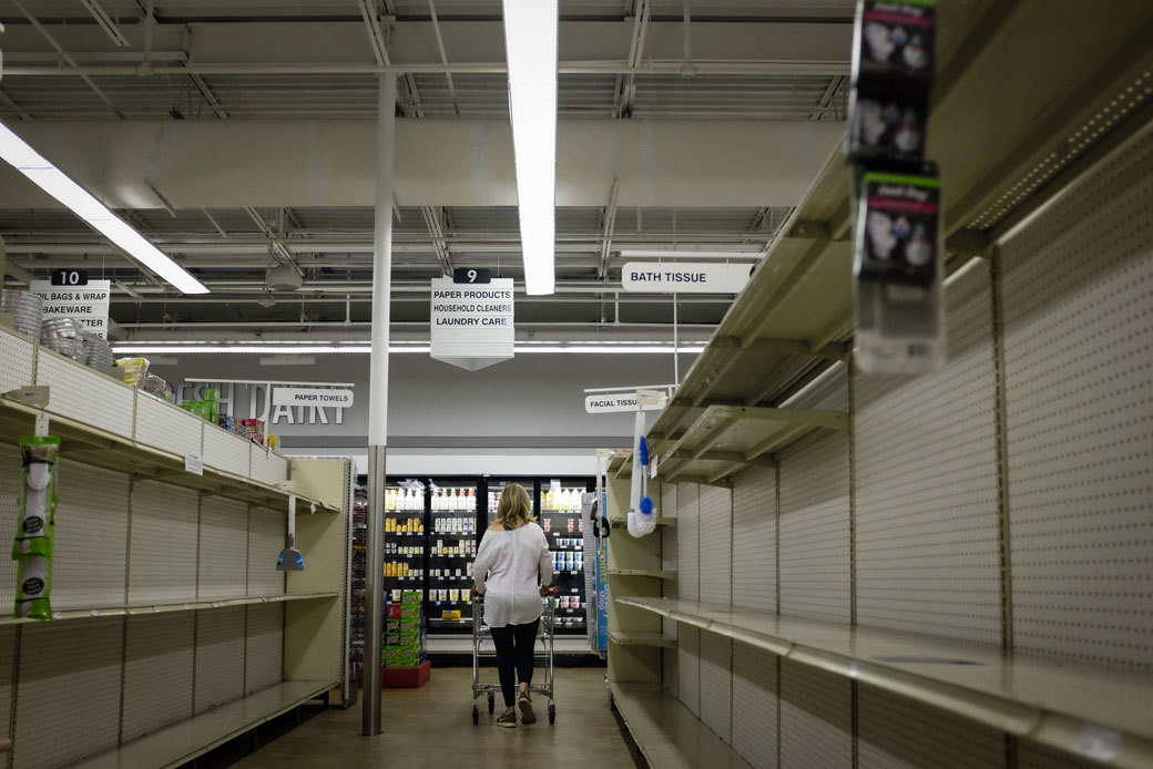 A woman walks down an aisle with partially empty shelves at a supermarket in Miami, Florida, on March 20, 2020. (Getty/Marco Bello)