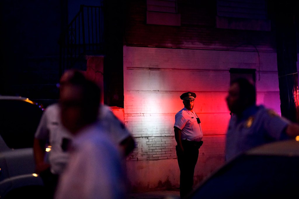 A police officer monitors activity near a residence while responding to a shooting.