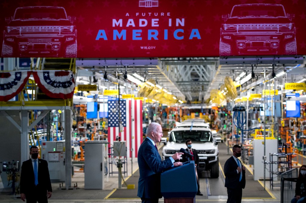 Photo shows the president standing at a podium in front of rows of electric vehicles.