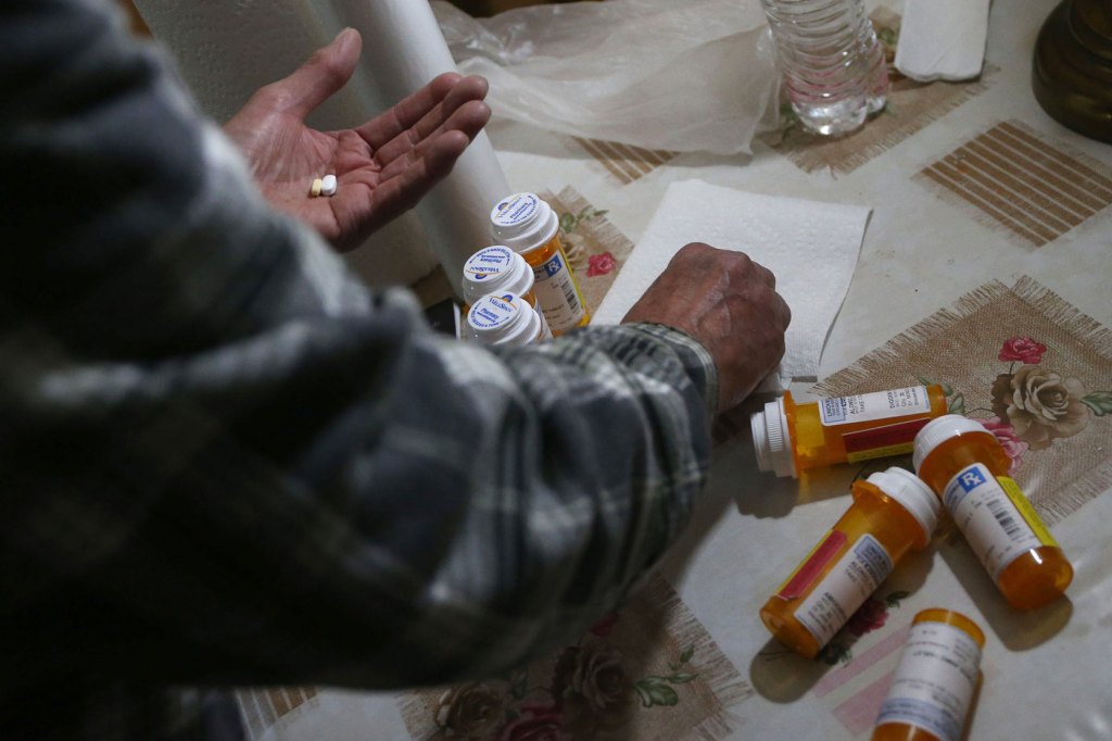 A man in Chicago prepares to take his prescription medicine after getting home from his job, holding and sorting various pills.