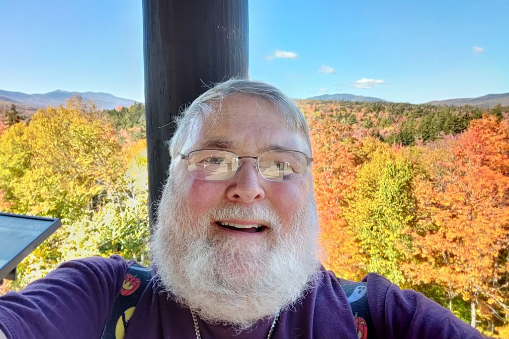 Gene Faltus smiles for a selfie in front of autumn foliage.
