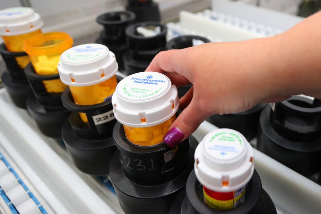 Filled prescription pill bottles are prepped on an automated line for packaging and shipping.
