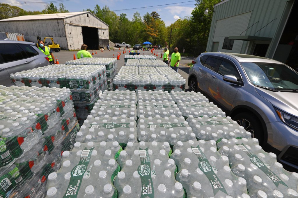 Four men stand next to stacked cases of plastic water bottles waiting to hand off to community members.