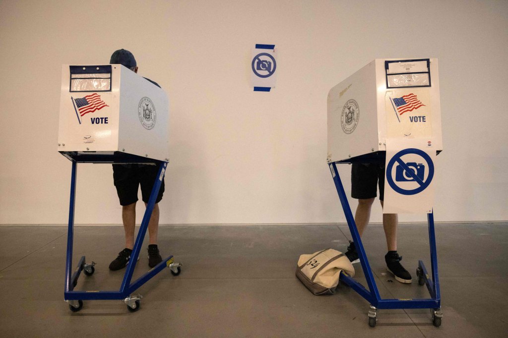 Photo shows two people at voting booths