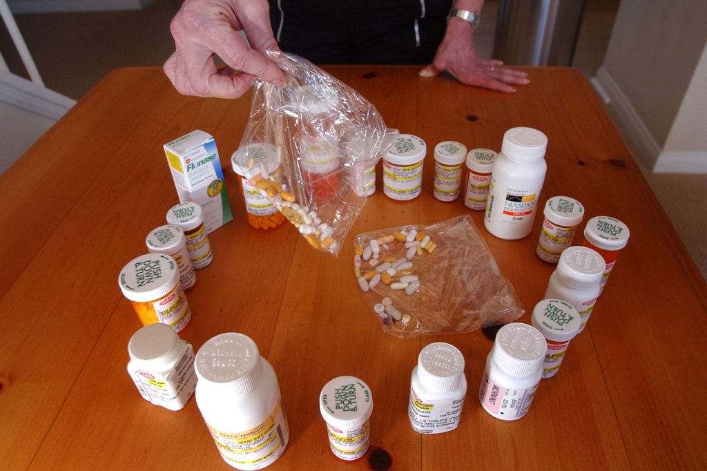 An older adult displays multiple bottles and plastic bags of prescription pills.