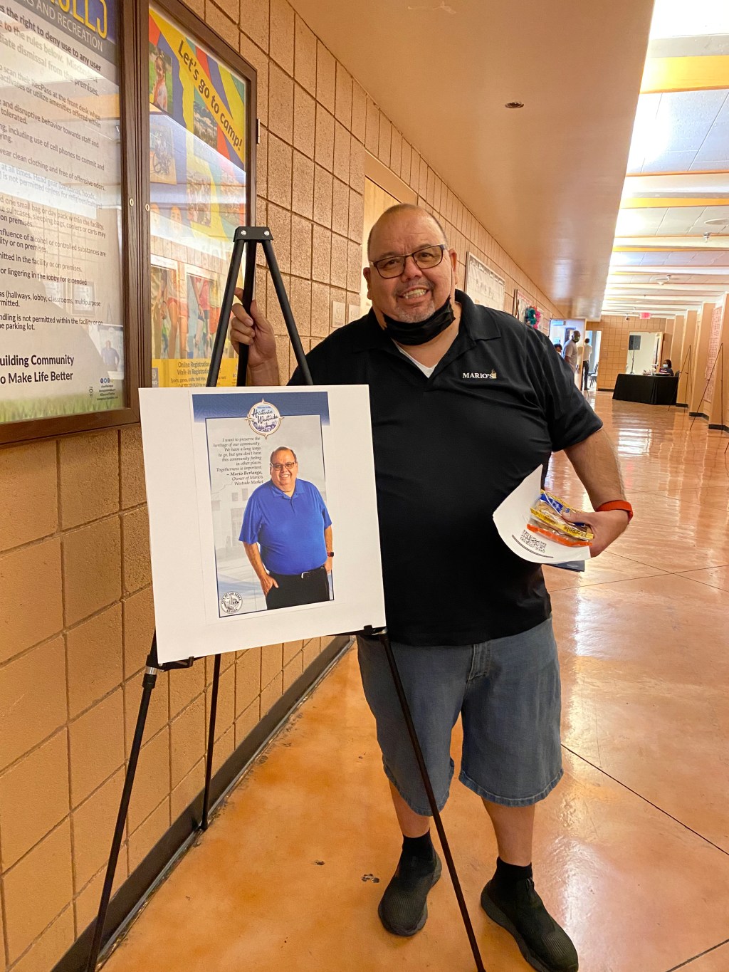 Mario Berlanga Jr. stands smiling next to a poster of himself quoted on the importance of businesses that are by and for the community.