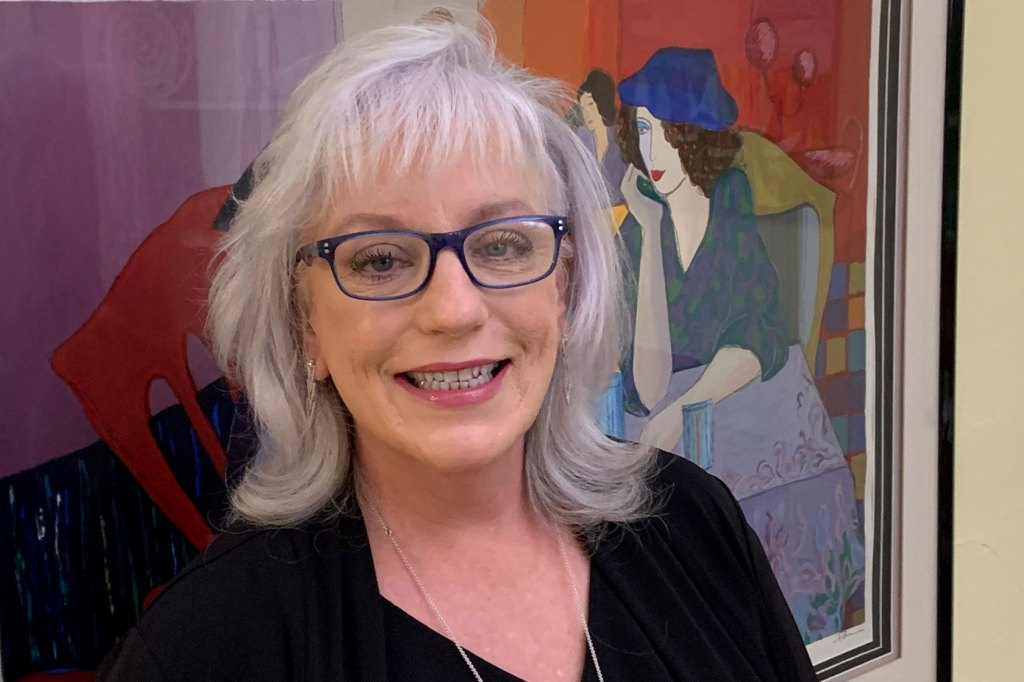 Photo shows Connie Grady smiling at the camera in front of a painting