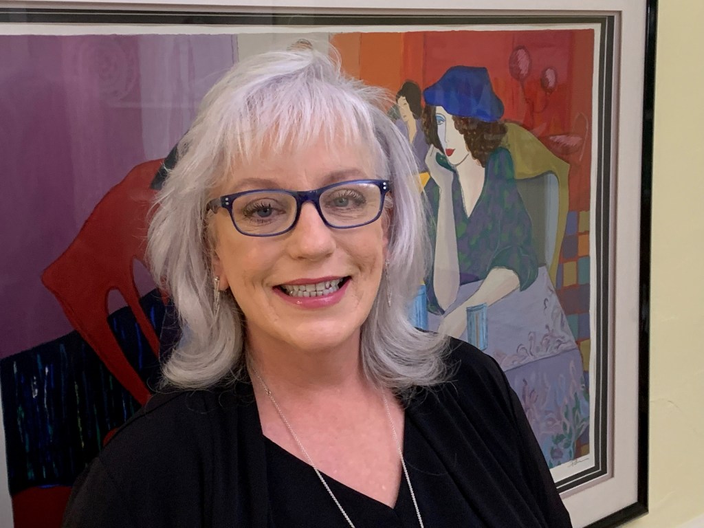 Photo shows Connie Grady smiling at the camera in front of a painting