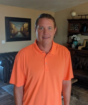 Photo shows David Ulfers smiling at the camera wearing an orange shirt
