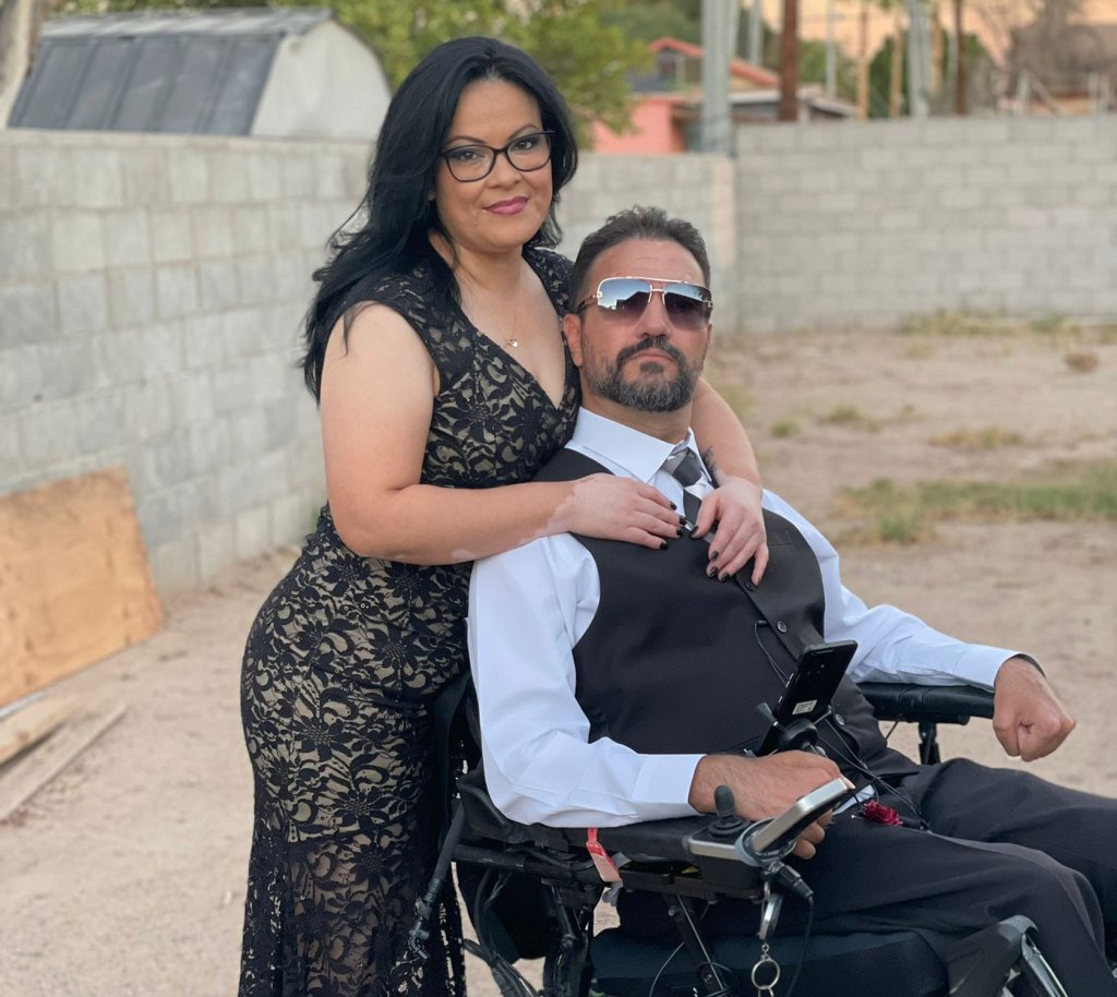 Photo shows Marcos Castillo, who uses a wheelchair, and his girlfriend, standing behind him, smiling at the camera wearing formal clothing.
