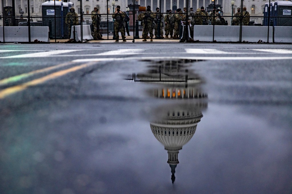 Capitol building reflected in puddle in foreground and troops in background