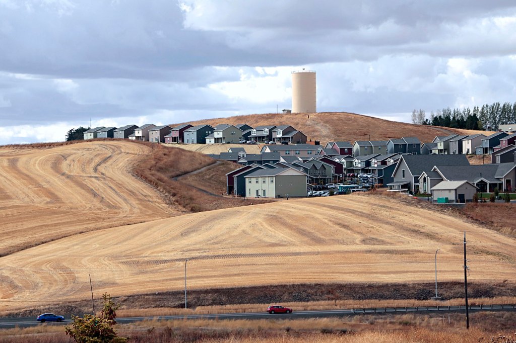 Photo shows a group of newly constructed houses closely bordering farmland.