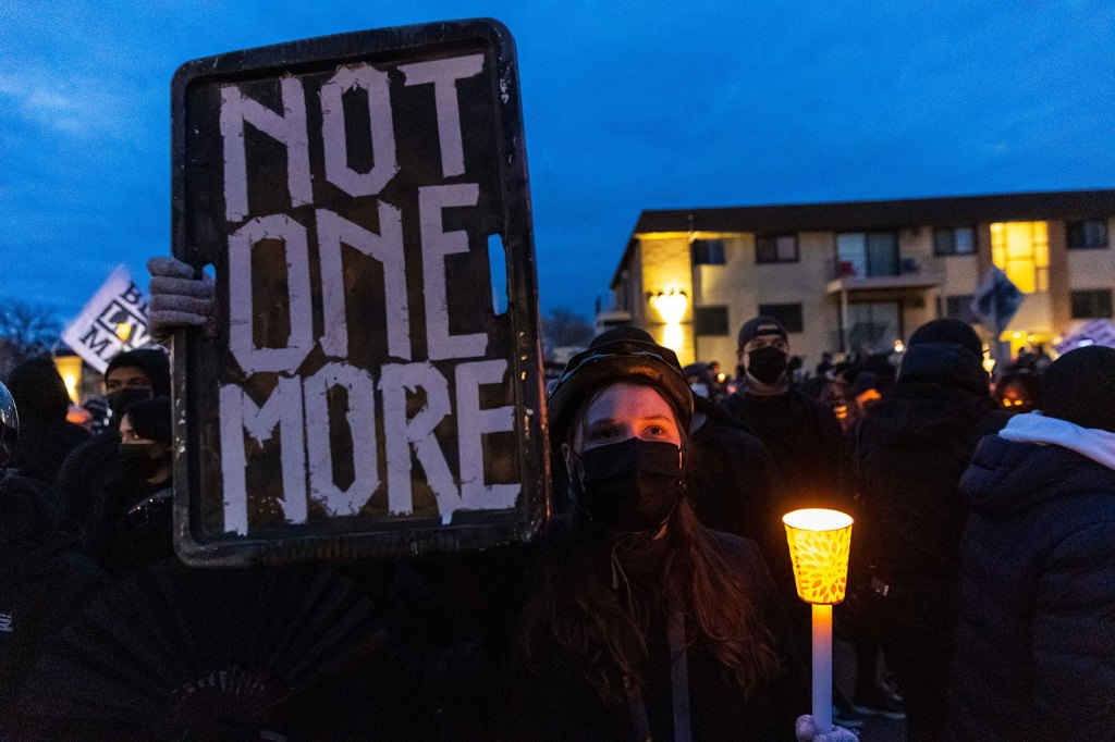 Photo showing a woman holding a candle and a sign that reads 