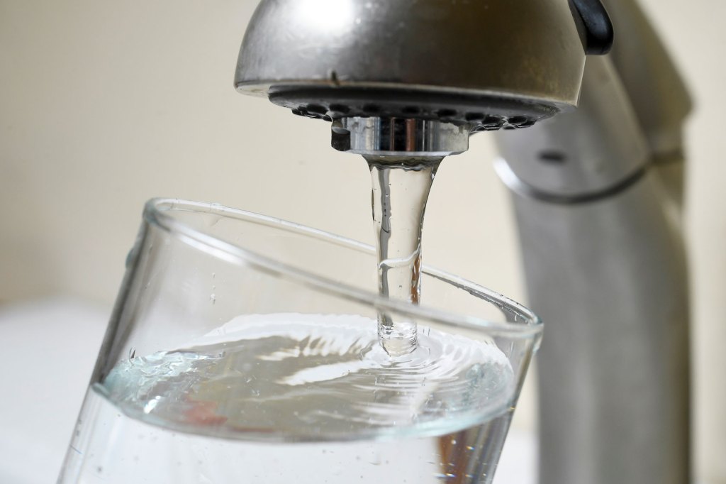 A faucet fills a glass of water to the brim.
