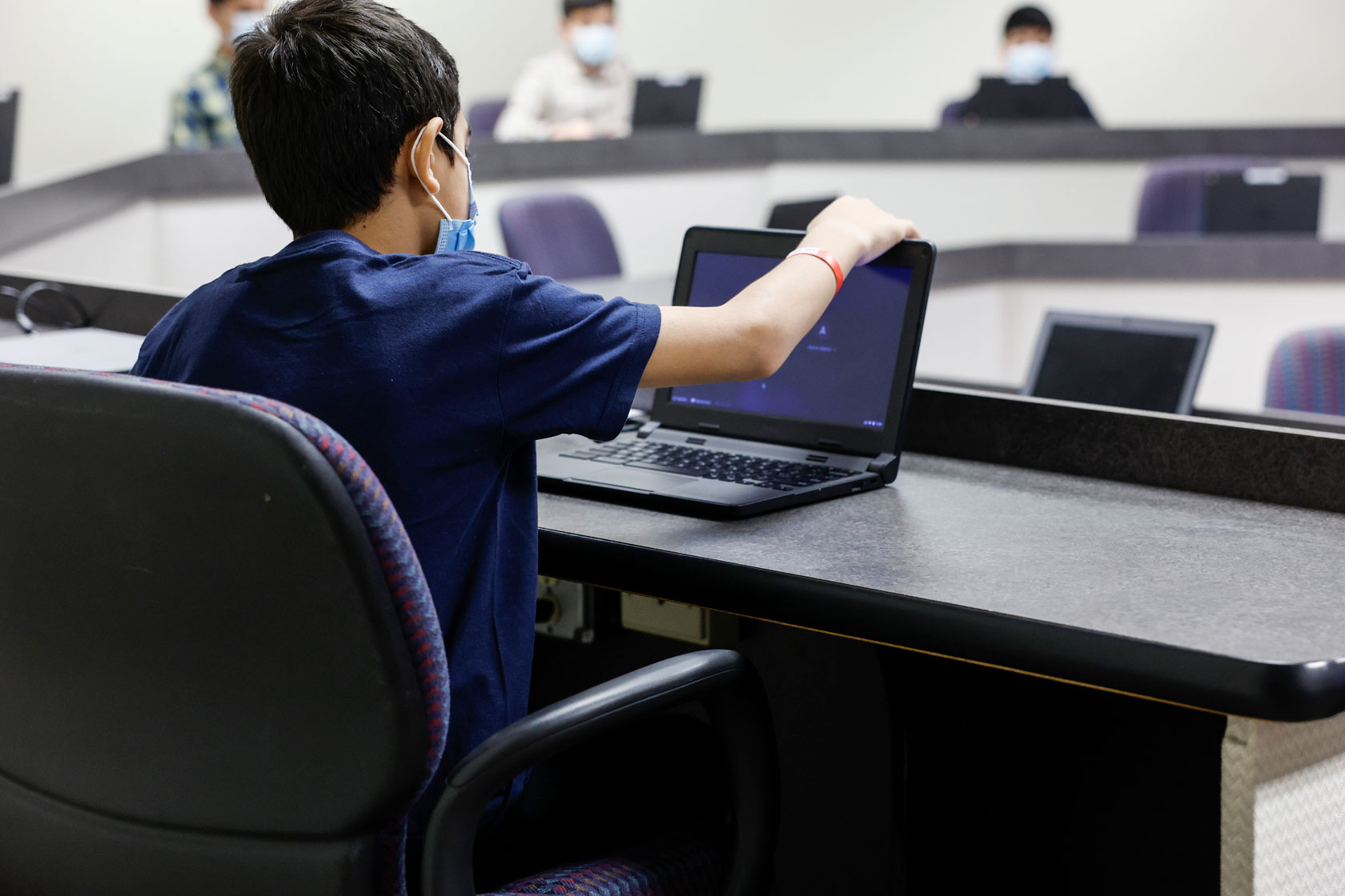 A boy opens his laptop in a computer classroom.