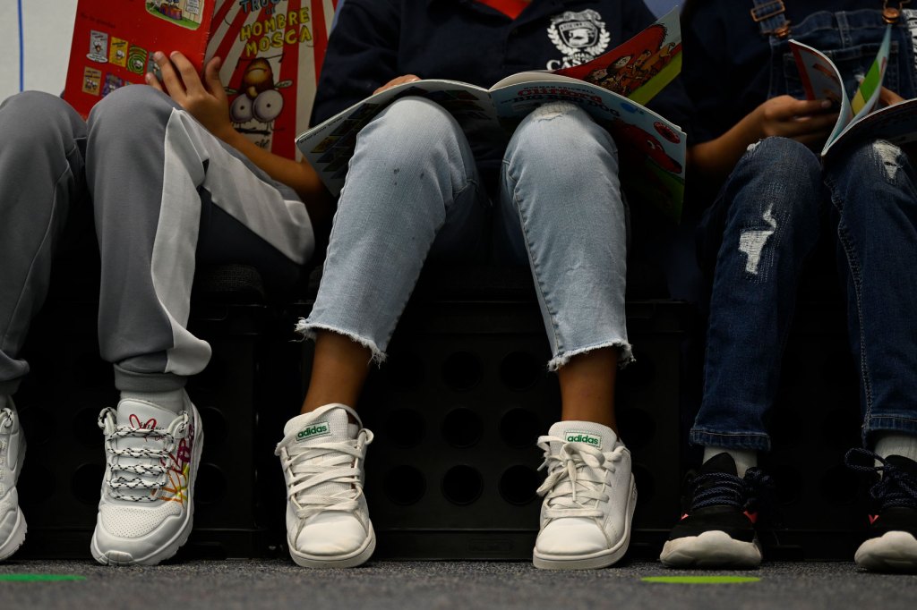 Elementary school-aged children sit in a row with books on their laps.