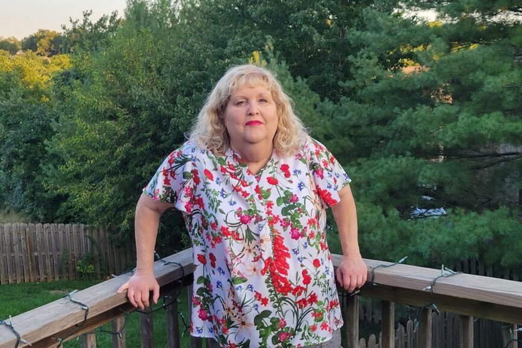 Photo shows Robin Craycroft wearing a colorful, floral shirt standing on a deck with green trees in the background