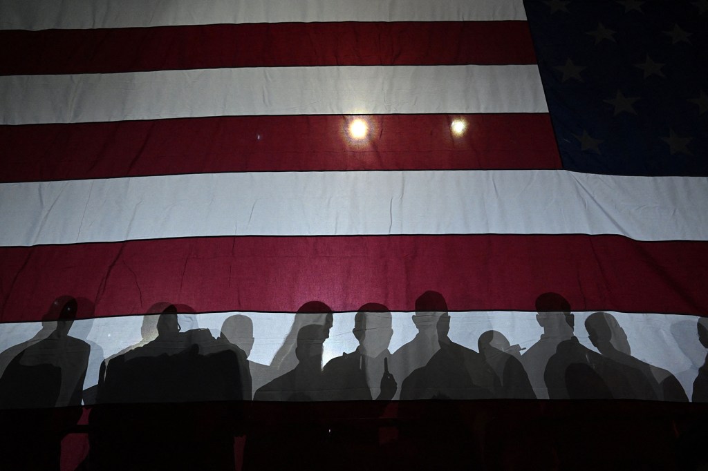 People in shadow behind American flag