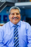 Photo shows Felix Ramirez wearing a blue shirt with a striped blue tie smiling at the camera.