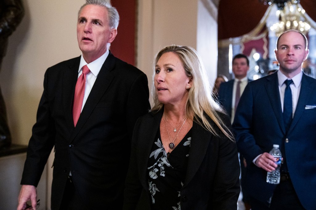 Photo shows Kevin McCarthy wearing a black suit and red tie walking alongside Marjorie Taylor Greene who wears a black dress and sweater