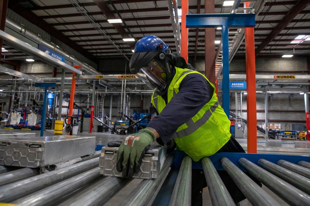 A technician places electric vehicle batteries on a conveyer belt at a recycling plant.