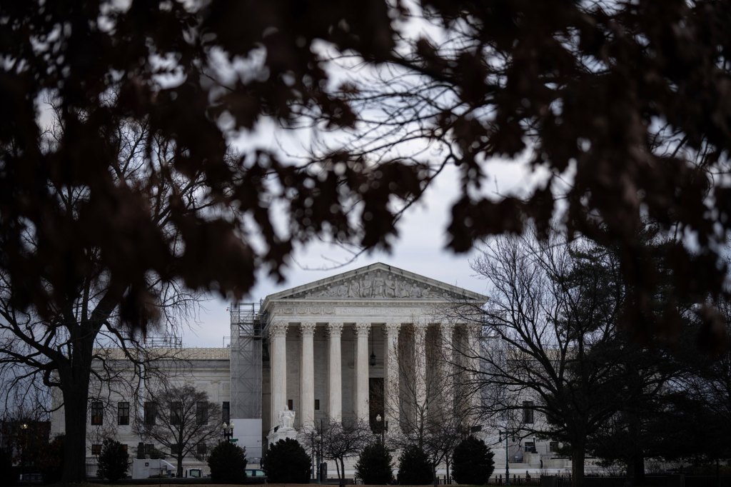 The U.S. Supreme Court building stands lies behind a foreground of trees.